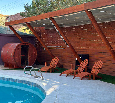 A poolside area with a wooden structure, a barrel-shaped sauna, and orange chairs.
