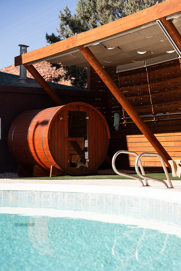 A wooden sauna next to a pool with a grassy area in between.