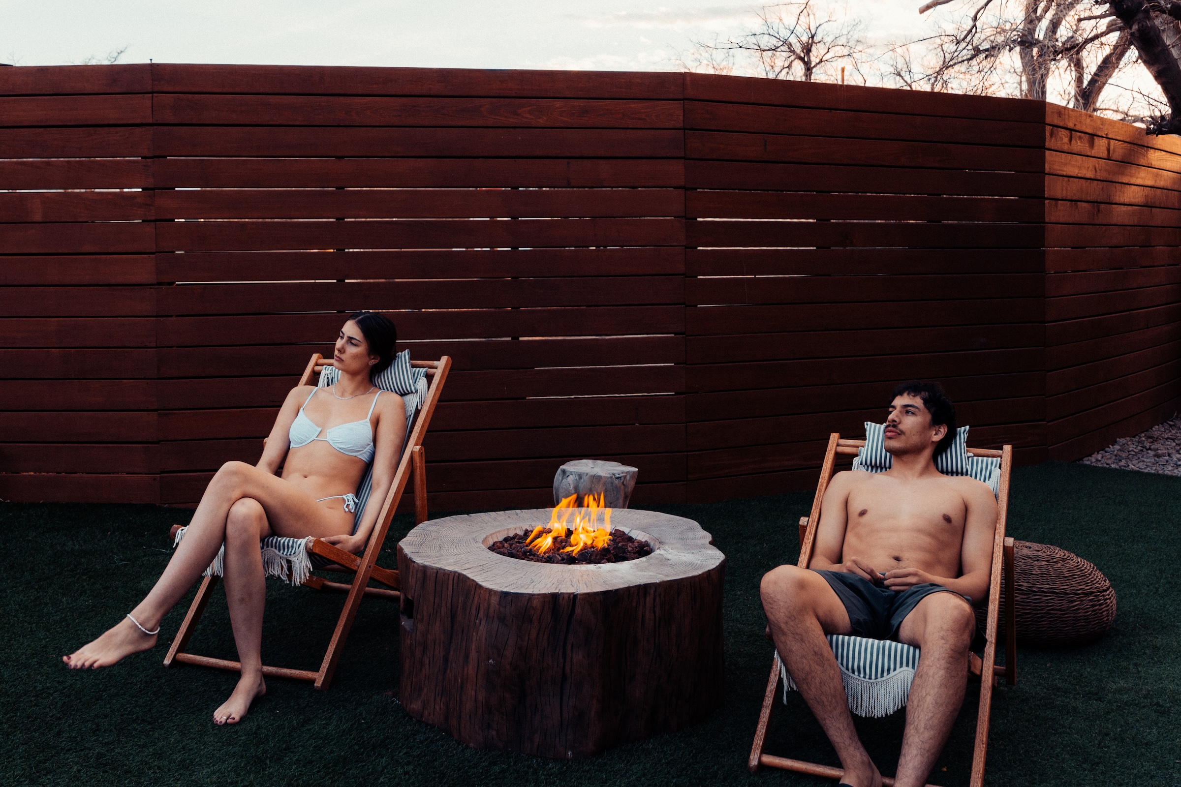 A man and a woman relax in swimsuits next to a firepit