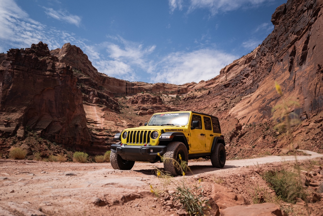 A Jeep Wrangler on a desert road surrounded by red rocks